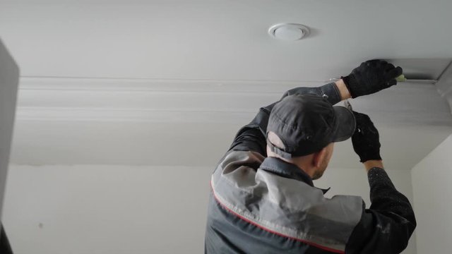 the man is doing repairs in the apartment, the person is painting with a tassel plaster molding on the ceiling