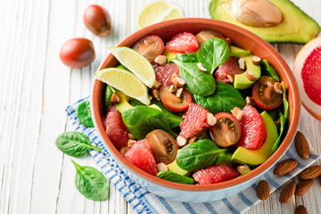 Fresh salad with spinach, avocado, tomatoes, grapefruit and almonds on white wooden background.