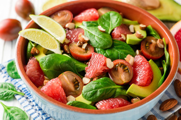 Fresh salad with spinach, avocado, tomatoes, grapefruit and almonds on white wooden background.