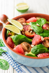 Fresh salad with spinach, avocado, tomatoes, grapefruit and almonds on white wooden background.