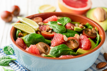 Fresh salad with spinach, avocado, tomatoes, grapefruit and almonds on white wooden background.