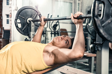Man lies on the gym bench and prepares for barbell exercises