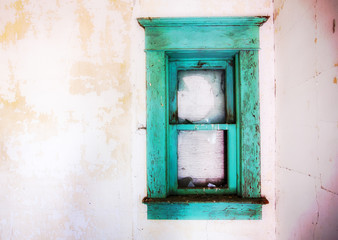 A wide vintage beautiful green wood frame surrounding a broken window in a decaying white interior wall of a house