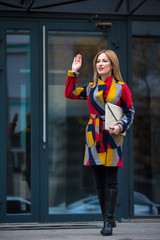 Full length portrait of smiling lady gesturing arm while standing near modern building. End of work concept