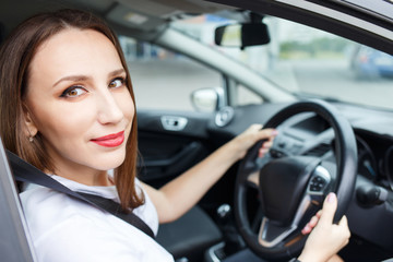 Obraz na płótnie Canvas Young woman in white shirt driving car on the road. Hispanic girl steering wheel in auto