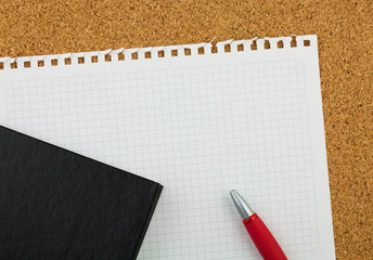 Empty square sheet of white paper wrested from notepad for your text. There are black notebook, red pen and cork board background.