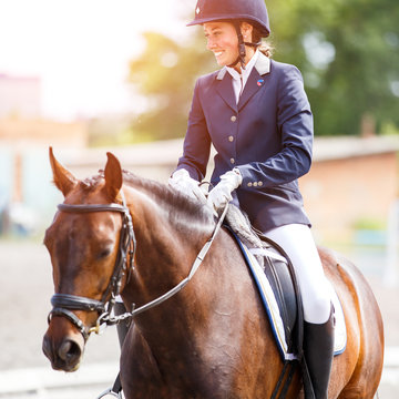 Young happy woman on her bay horse after dressage test on equestrian competitions