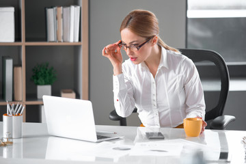 Portrait of serious girl watching at notebook computer while sitting at table in apartment. Profession concept