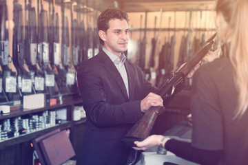 Salesman in gun shop showing rifle to female client