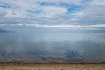 Clear crystal water of Lake Baikal in calm weather . Blue sky and clouds reflection.