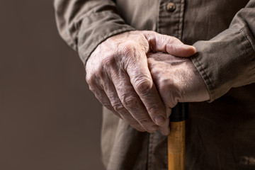 Close up of elderly hands in wrinkles holding walking stick. Isolated on grey background