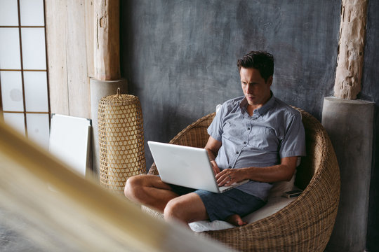 Man In His 30's Working On Laptop In Chair On Vacation