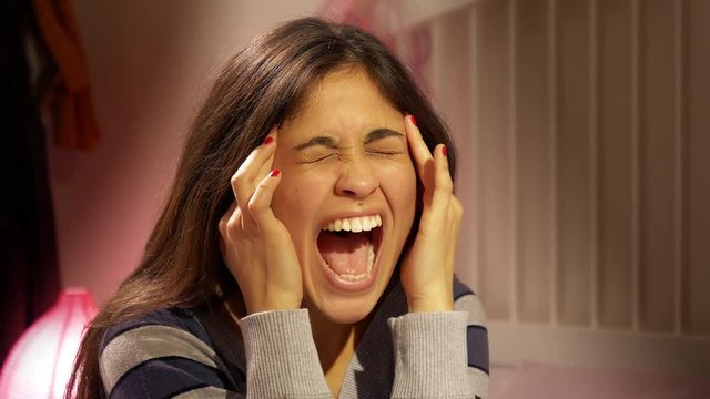 Hispanic woman in bed with strong headache at night screaminf for pain closeup
