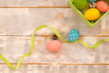 Multicolored Easter eggs in a wooden box, ribbons on a wooden background. Country style. Flat lay