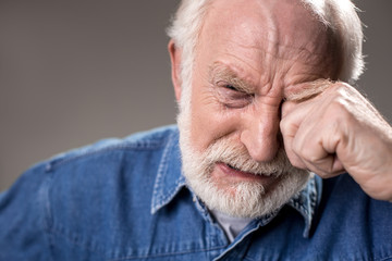 So lonely. Portrait of depressed male pensioner looking at camera and crying. Isolated on grey background