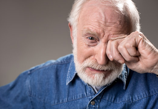 Portrait Of Upset Old Man Rubbing His Eye While Crying. Isolated On Grey Background