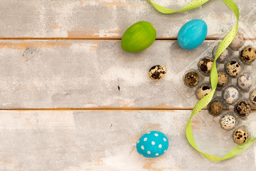 Multicolored Easter eggs in plastic box and ribbons on a wooden background. Country style. Flat lay. Space for text