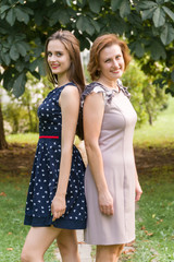 Closeup Portrait of Adult Daughter and Mother Outdoors. Pretty Brunette and Her Mom are Looking at the Camera in the Park in Summer.