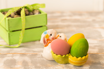 Multicolored Easter eggs in a wooden box, rabbit, ribbons on a wooden background. Country style.