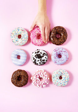 Various donuts on a pink background. A woman's hand taking one. Sweetness happiness conception.