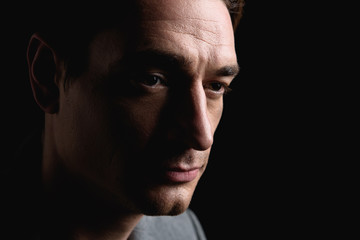 Desperation. Close-up of face of hopeless unhappy young guy is standing and looking aside sorrowfully. Isolated on dark background