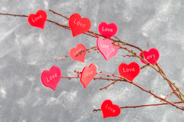 Red hearts with an inscription Love hang on branches on a gray concrete background. Love tree. The...