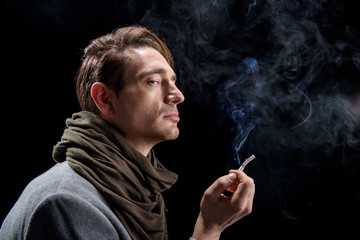 Melancholy. Side view profile of unhappy young elegant man is standing with cigarette. He is looking aside thoughtfully while being in cloud of white smoke. Isolated background