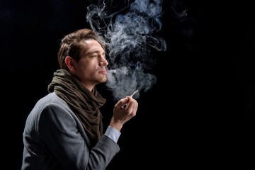Depression. Side view profile of sad young stylish man is standing and enjoying cigarette. He is...