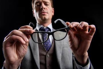 Low angle of confident stylish businessman is standing and frowning while looking at eyeglasses in his hands with concentration. Isolated background. Selective focus