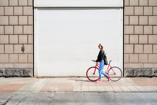 Woman walking with bicycle along the street.