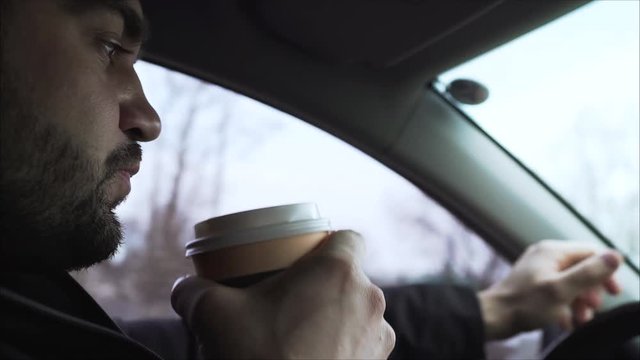  the guy a the guy at the wheel of the machine drinks coffee. The guy drinks coffee in the car. The guy is driving in the car and drinking coffee.