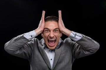 Full of rage. Portrait of annoyed angry young businessman is expressing discontent and shouting loud while touching his head and looking at camera in wide-eyed. Isolated background