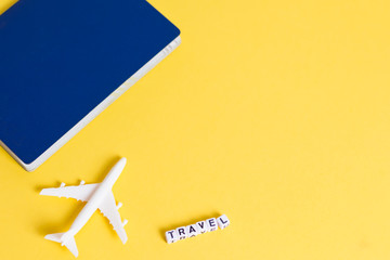 White blank model of passenger plane, passport and word TRAVEL on yellow background. Copy space