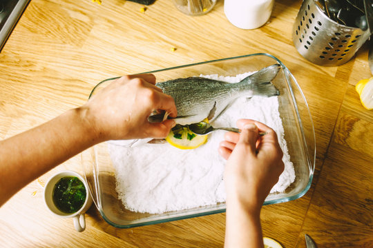 Cooking a fresh gilthead seabream with lemon, garlic and herbs, covered with salt
