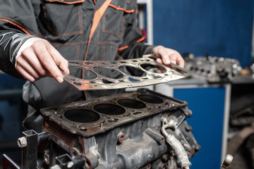 Sealing gasket in hand. The mechanic disassemble block engine vehicle. Engine on a repair stand with piston and connecting rod of automotive technology. Interior of a car repair shop.