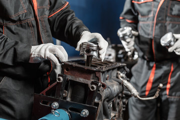two worker, the mechanic installs a new piston. Disassemble engine block vehicle. Motor capital...