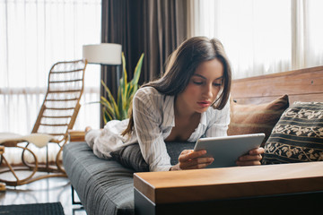 Young Pretty Brunette Lying on Sofa and Watching Movie on Digital Tablet