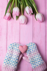 Knitted gloves, pink heart and pink tulips on a wooden background. Valentine's Day background. Top view, free space