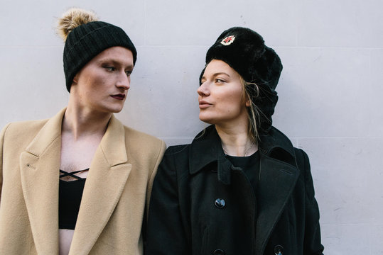 Two friends in winter hats look at one another