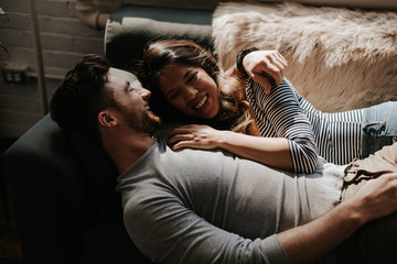 Attractive young interracial couple cuddling on couch in trendy loft apartment
