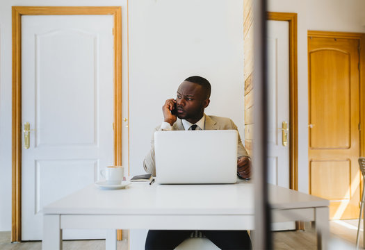 Young African man talking by phone and working with a laptop in