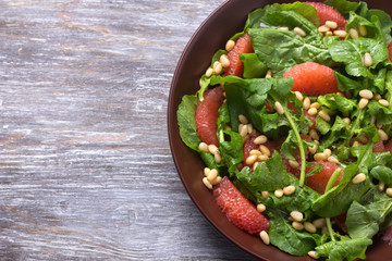 Fresh salad from arugula with grapefruit and pine nuts on a wooden background. Healthy delicious food