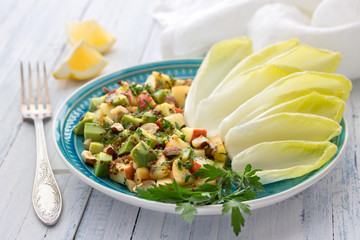 Fresh leaves chicory with a salad of avocado, apple, nuts and parsley on a blue wooden background. Healthy, vegan food. Selective focus