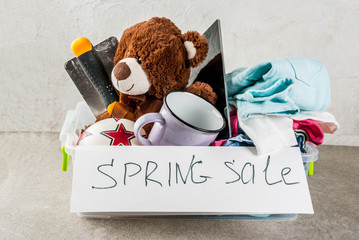 Plastic spring sale box with toys, clothes gadgets and tools, white grey background copy space