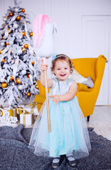 Pretty little girl in blue dress looks funny posing in cosy room decorated for winter holidays