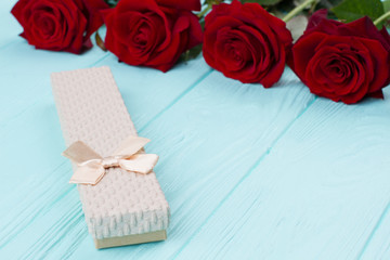 Roses and little gift box. Flowers and box with jewelry on blue wooden background. Exclusive gift for Valentine Day.