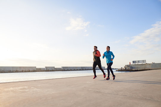Athletic couple running along pier in sunlight.