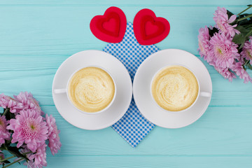 Beautiful composition of Valentines breakfast. Two cups of cappuccino, red Valentine hearts and flowers.