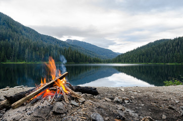Landscape of a campfire in a peaceful lake valley. - obrazy, fototapety, plakaty