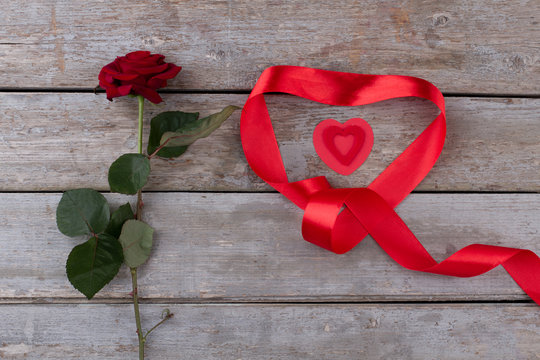 Beautiful red rose for Valentines Day. Composition of red rose and ribbon in heart shape on old wooden background. Love and romance.